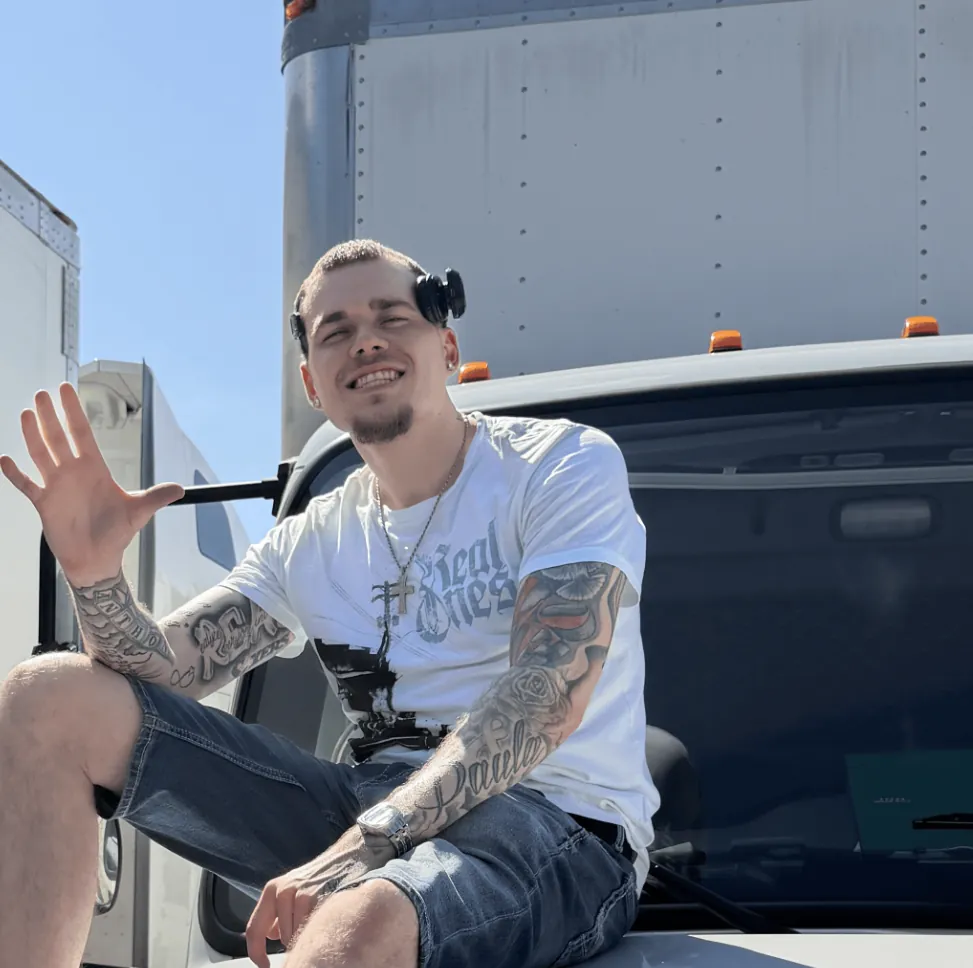 Anthony Schulz, founder of Move Makers, sitting on the hood of a box truck and waving